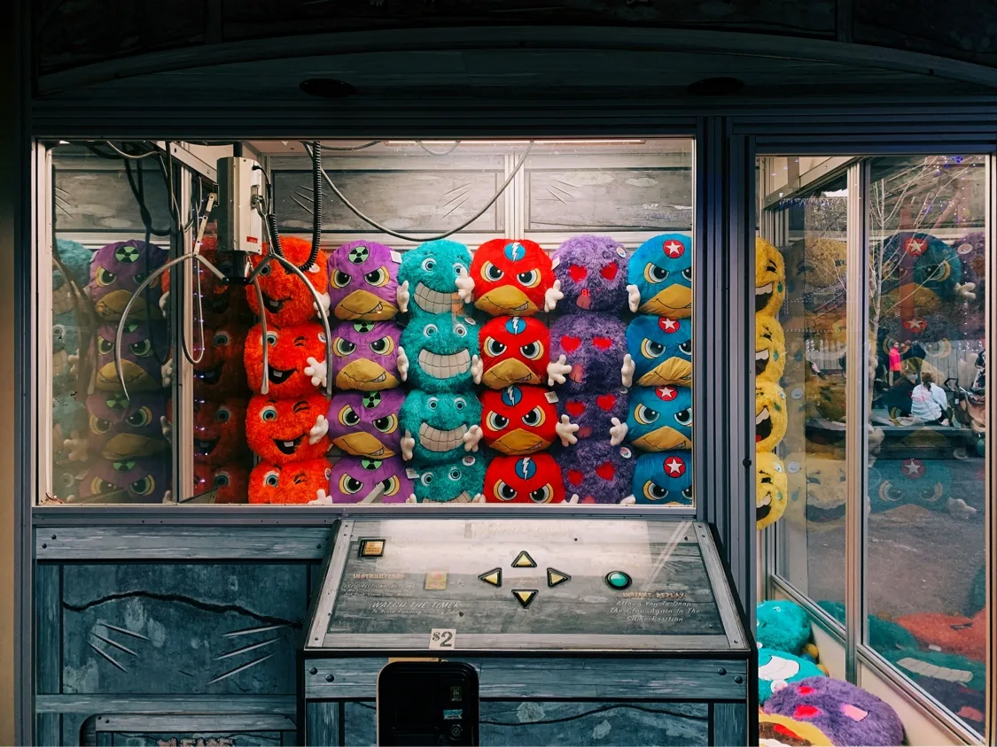 An arcade claw machine stacked with colourful plush toys